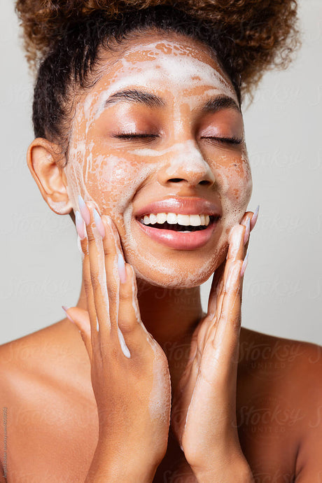 Woman applying a facial mask with a neutral background
