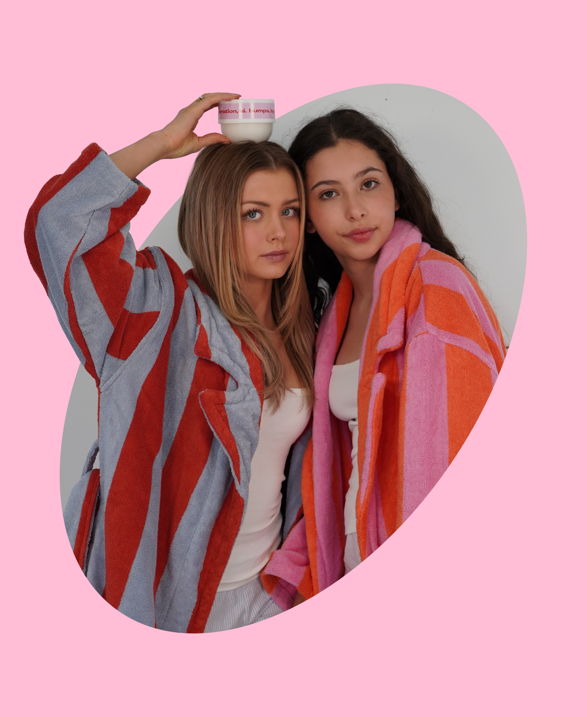 Two women in colorful robes holding a cup against a pink background