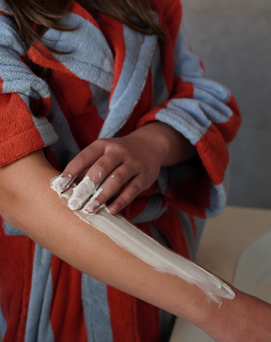Person applying cream to their arm with a towel draped over their shoulder.