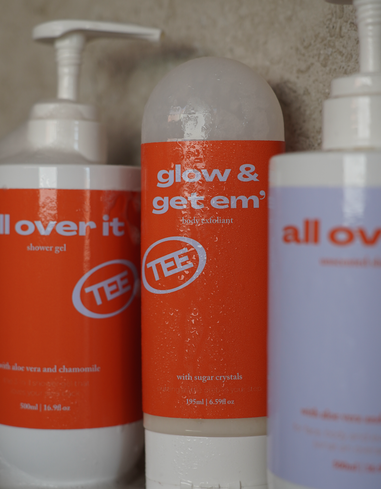 Three bottles of 'Tee' products including 'all over it', 'glow & get em', and 'all ov'.