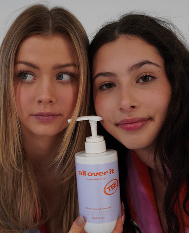 Two women holding a bottle labeled 'all over it' with a visible brand logo.