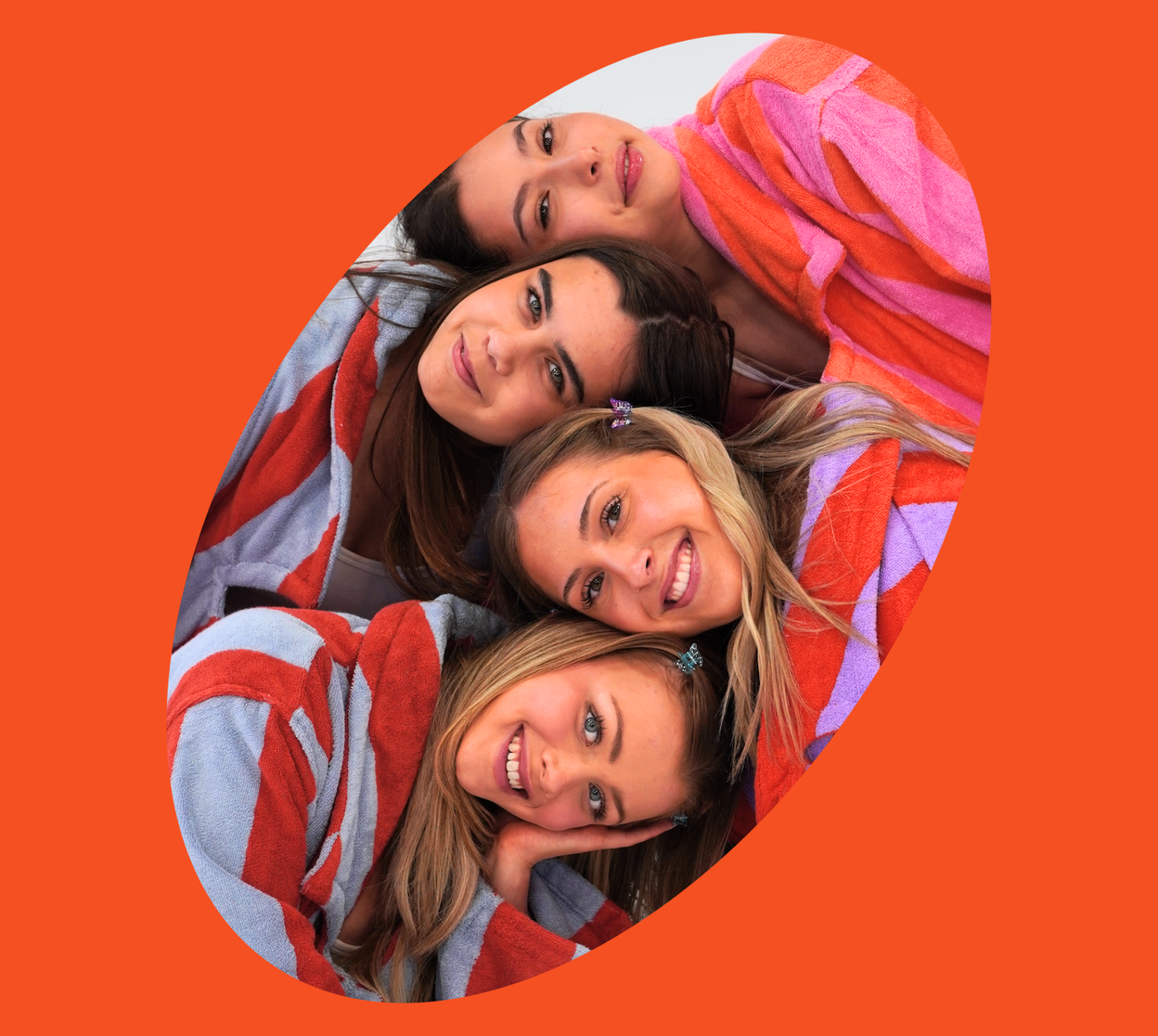 Four women hugging under a colorful blanket with an orange border
